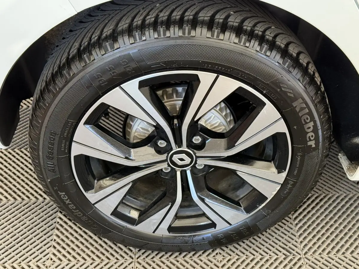 Gros plan sur la roue avant droite d’une Renault Clio blanche, jante alliage bicolore avec logo Renault central.