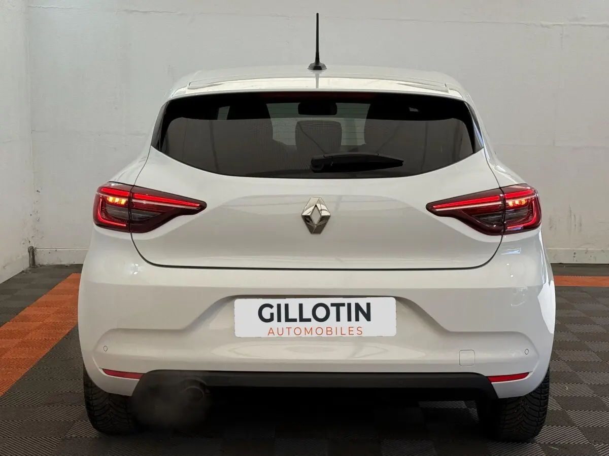Vue arrière d'une Renault Clio blanche Evolution TCe 100 GPL avec feux LED allumés dans un garage.