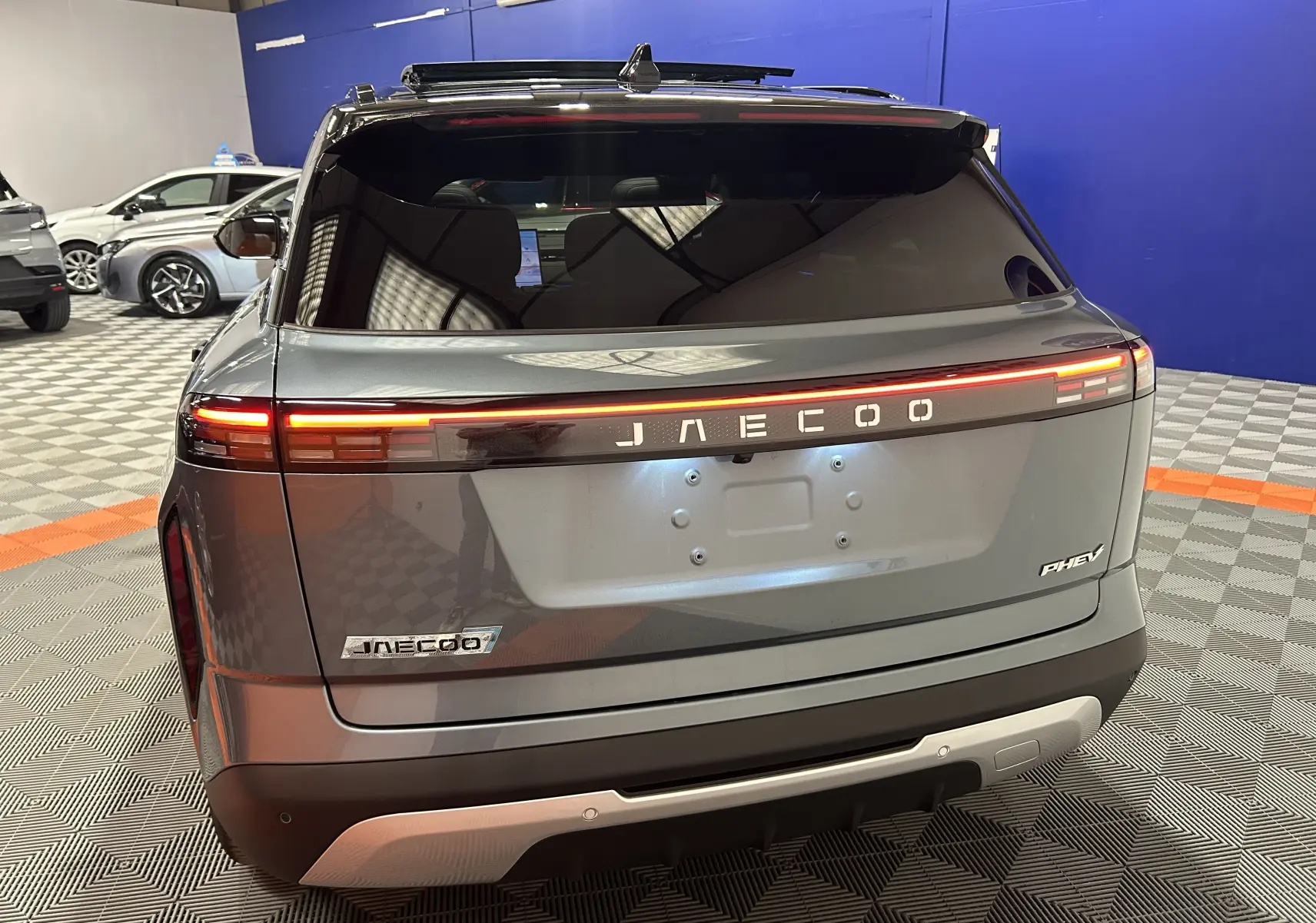 Vue arrière d'un JAECOO J7 olive grey metal avec feux LED continus et logo lumineux sur fond noir.