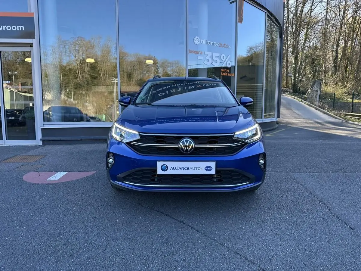Volkswagen Taigo bleu Recife vue de face, avec calandre noire et phares LED allumés devant showroom.