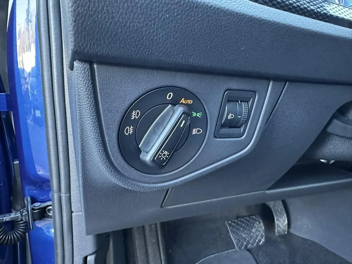 Gros plan sur le bouton de commande des phares à gauche du volant, intérieur noir avec portière bleu Recife visible.