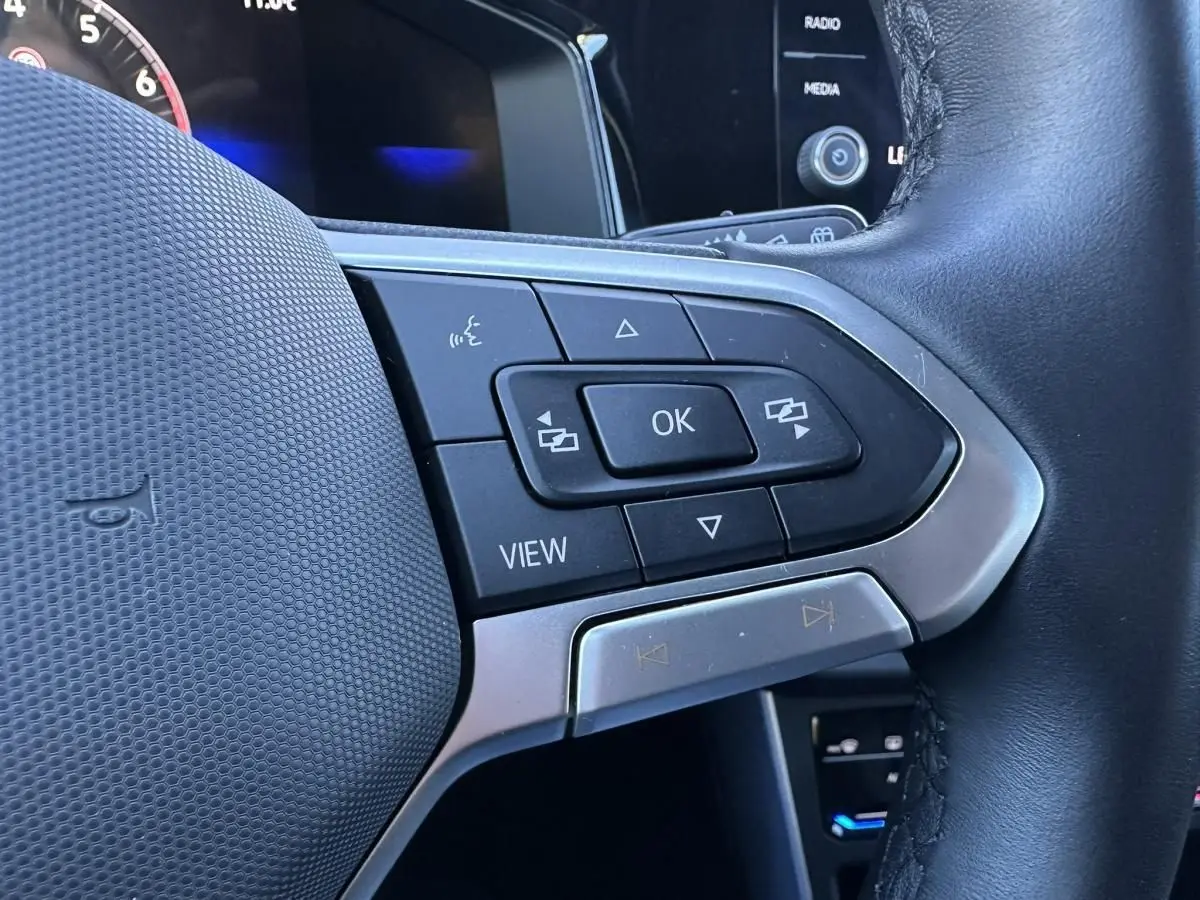Gros plan sur les commandes multifonctions au volant noir du Volkswagen Taigo Bleu Recife, côté gauche.
