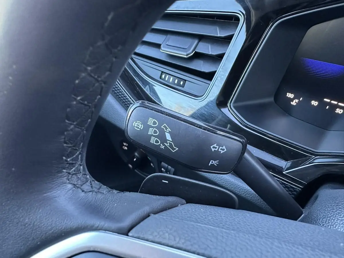 Gros plan sur le commodo gauche du volant en cuir noir du Volkswagen Taigo 2025, avec tableau de bord numérique en arrière-plan.