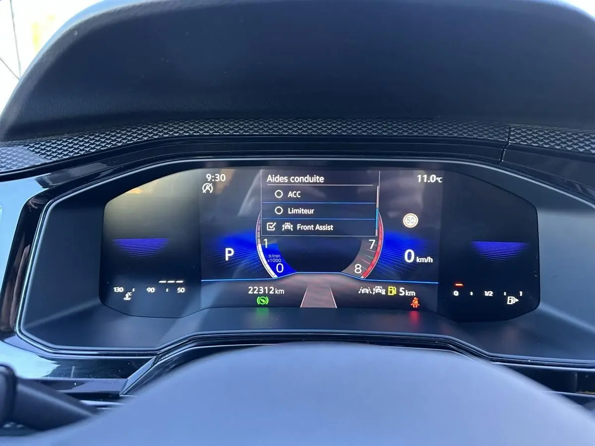Vue rapprochée du tableau de bord numérique du Volkswagen Taigo bleu Recife, affichant les aides à la conduite et la vitesse à 0 km/h.