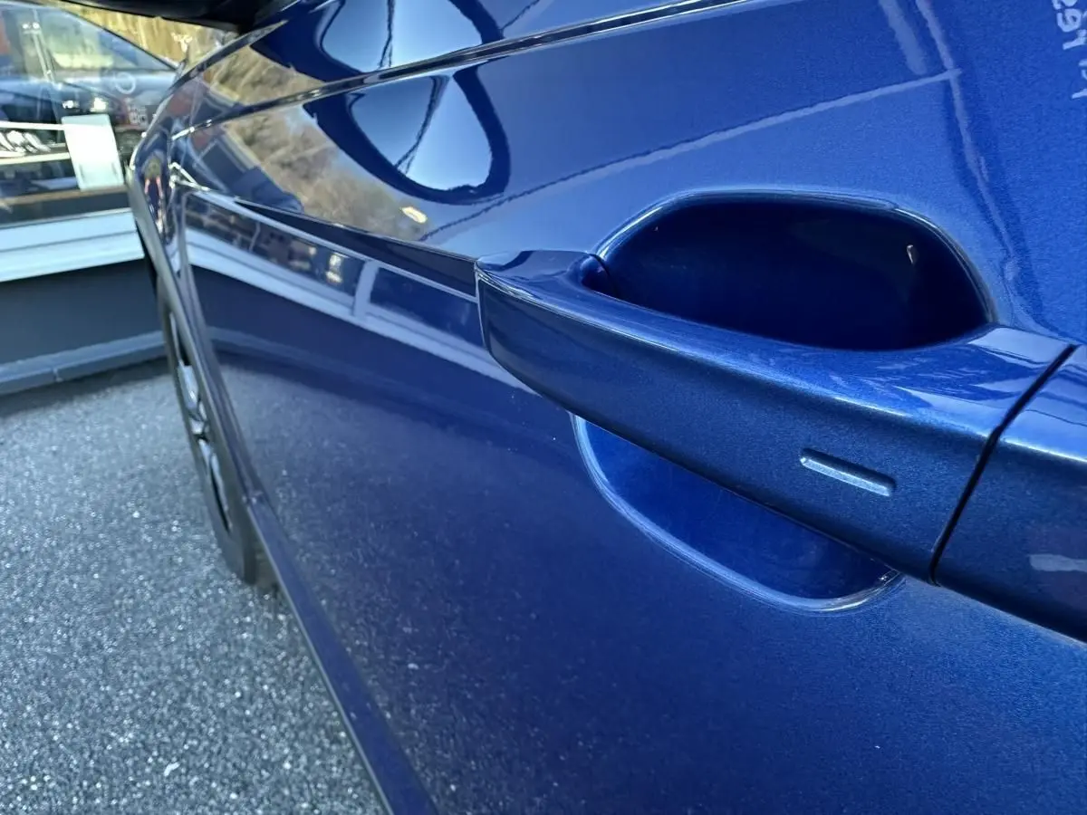 Gros plan sur la poignée de porte côté droit d’un Volkswagen Taigo 2025 bleu Recife avec peinture métallisée.