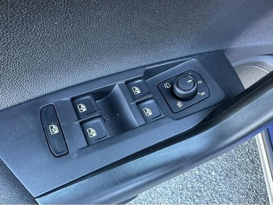 Vue rapprochée des commandes de lève-vitres et réglage des rétroviseurs sur la porte côté conducteur du Volkswagen Taigo bleu Recife.