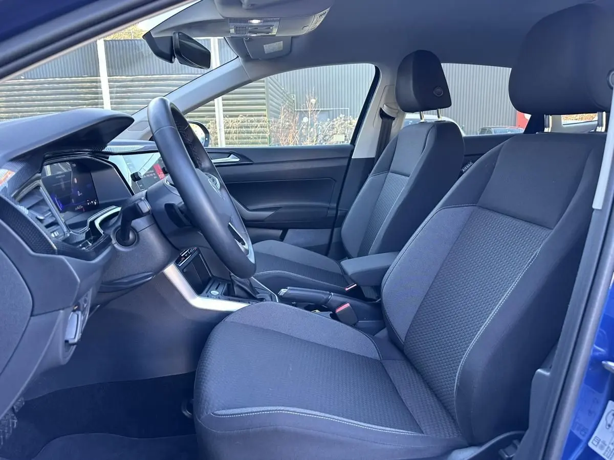 Vue intérieure côté conducteur du Volkswagen Taigo bleu Recife 2025, avec sièges tissu gris et accoudoir central.