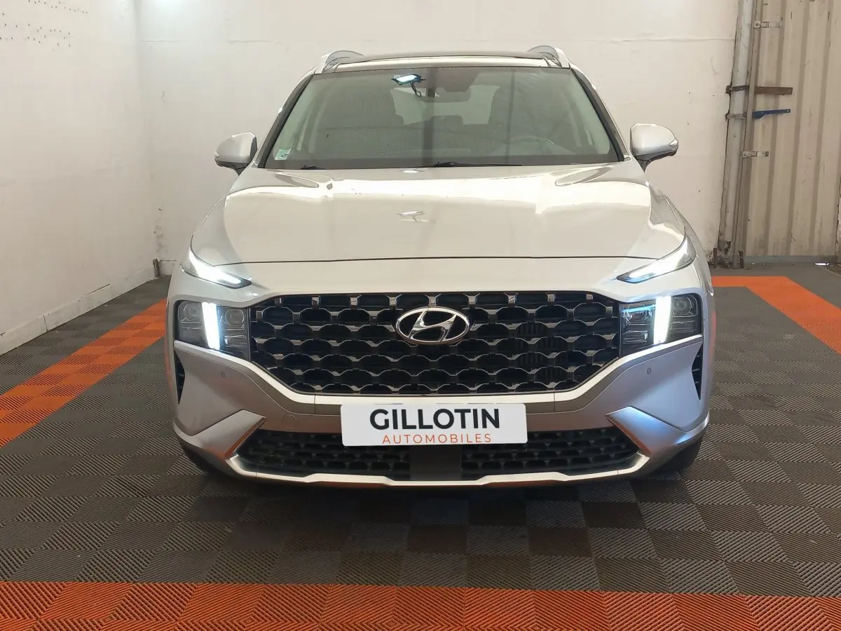 Vue frontale du Hyundai Santa Fe gris clair 2022 avec calandre noire et phares LED allumés dans un garage.