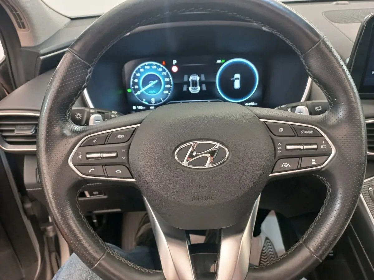 Vue rapprochée du volant cuir multifonctions du Hyundai Santa Fe 2022 avec tableau de bord numérique éclairé.