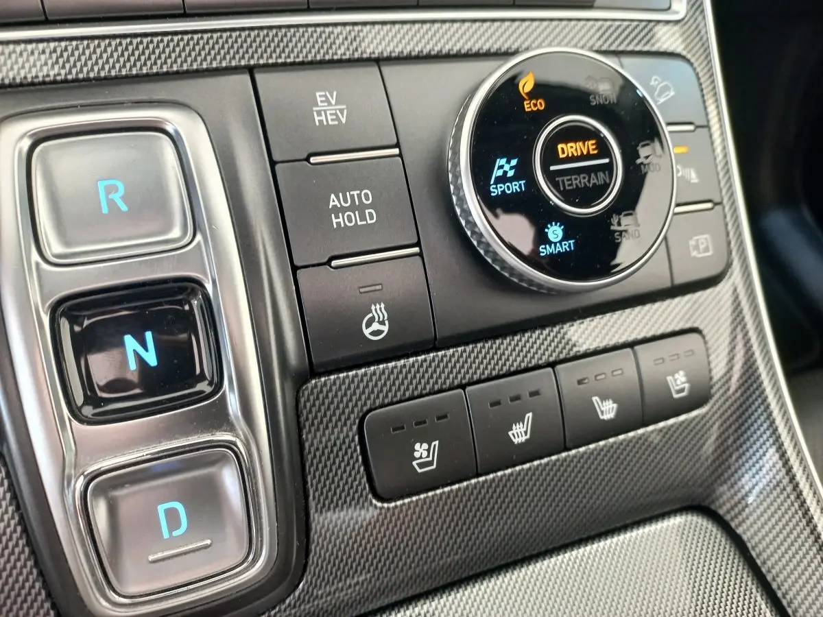Gros plan sur la console centrale du Hyundai Santa Fe 2022, boutons de boîte auto et sélection modes terrain sur finition carbone.