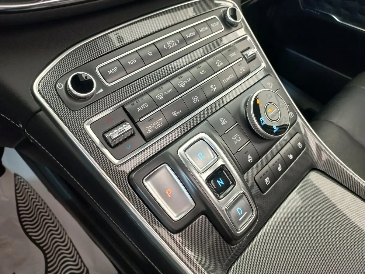 Gros plan sur la console centrale en carbone du Hyundai Santa Fe 2022 avec commandes de boîte auto et réglages climatiques.