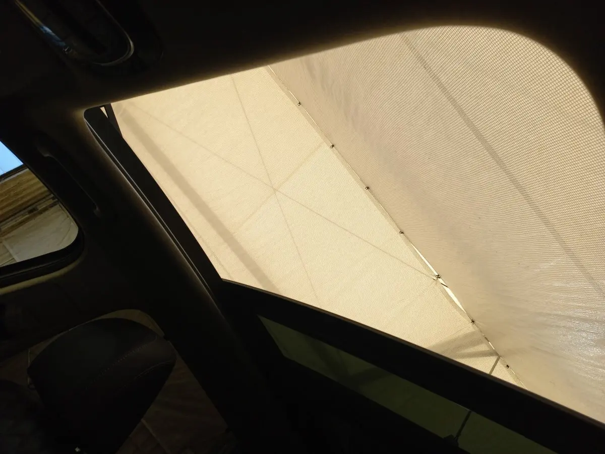 Vue intérieure du toit ouvrant électrique en verre du Hyundai Santa Fe gris clair, avec store déployé.