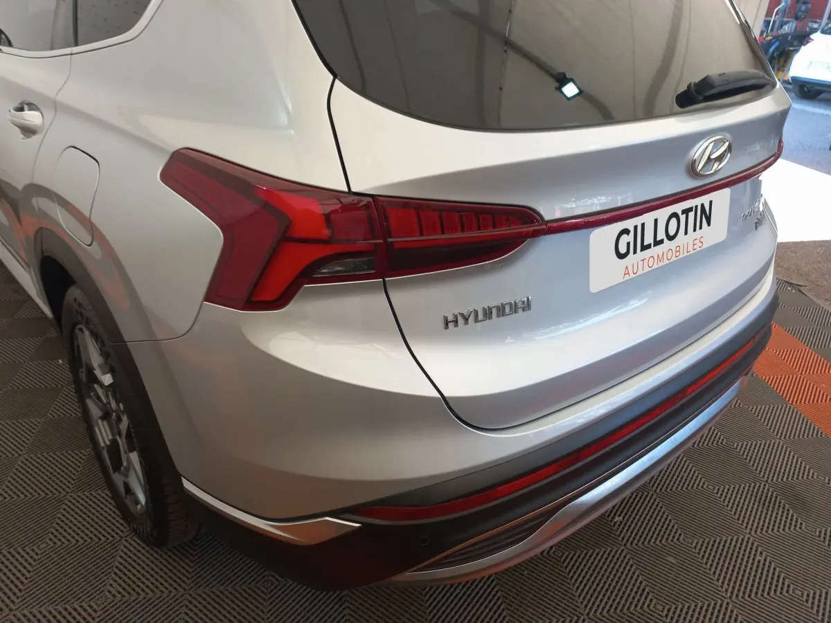 Vue 3/4 arrière droite d’un Hyundai Santa Fe gris clair avec feux arrière LED et logo visible.