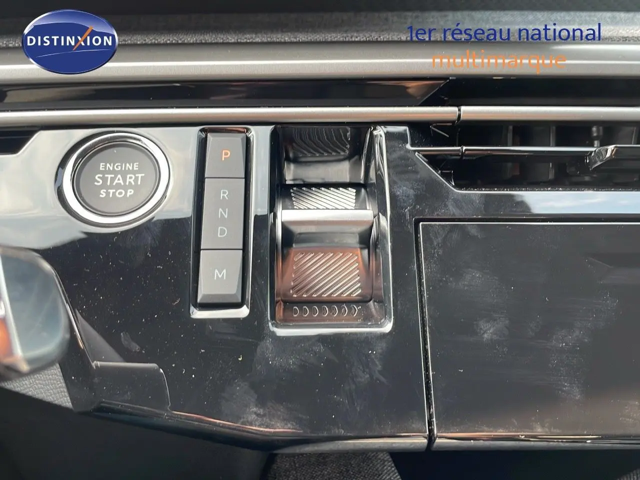 Gros plan sur la console centrale noire brillante du Peugeot 3008 Hybrid 2025 avec bouton start/stop et commandes de boîte automatique.