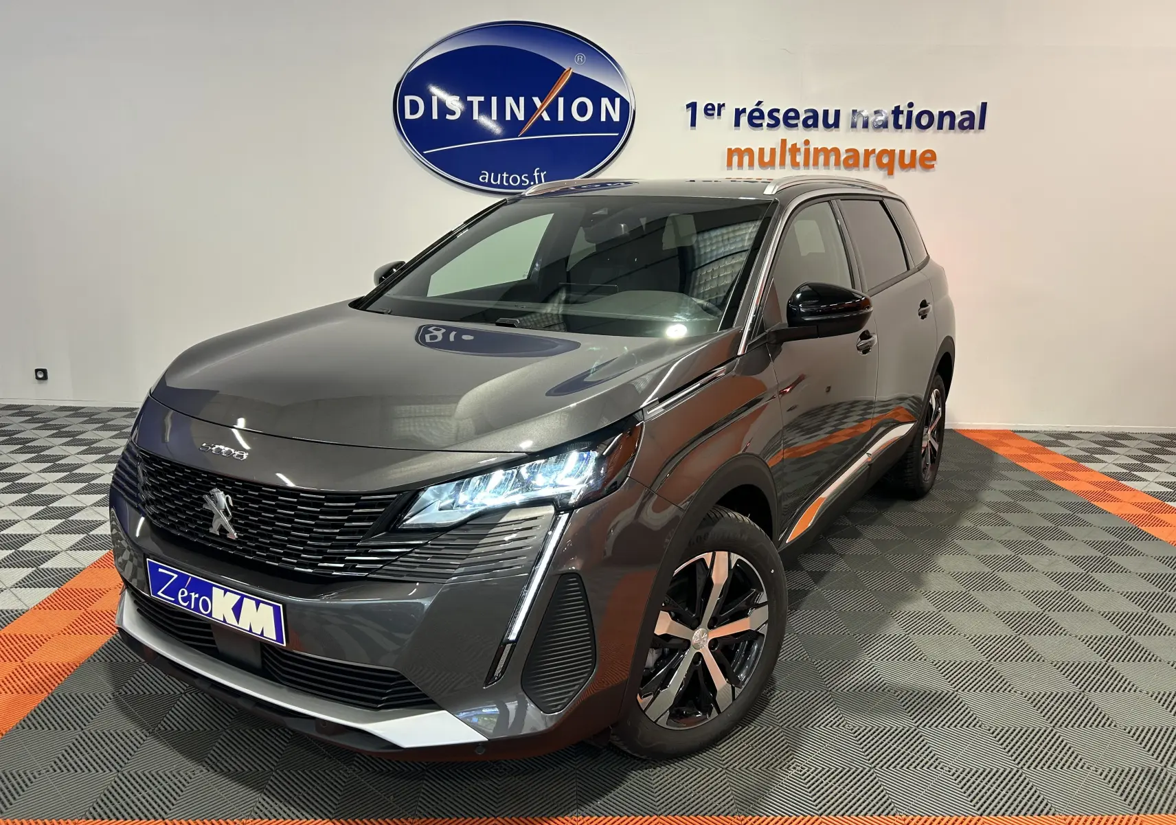 Peugeot 5008 Gris Platinium en 3/4 avant droit, avec phares LED allumés et jantes bi-ton visibles.