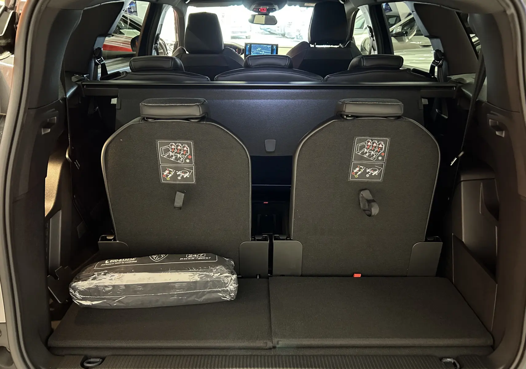 Vue arrière du coffre du Peugeot 5008 gris Platinium 2024 avec sièges rabattus et kit de sécurité visible.