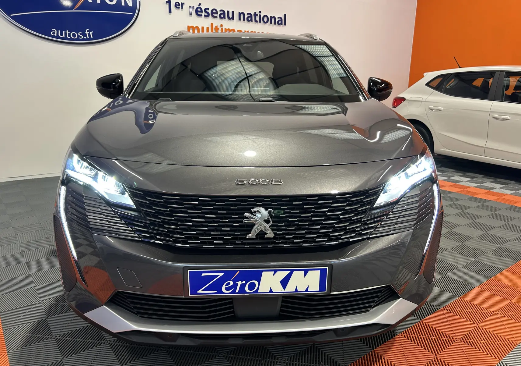 Vue frontale d'un Peugeot 5008 2024 gris Platinium avec phares LED allumés et calandre noire distinctive.