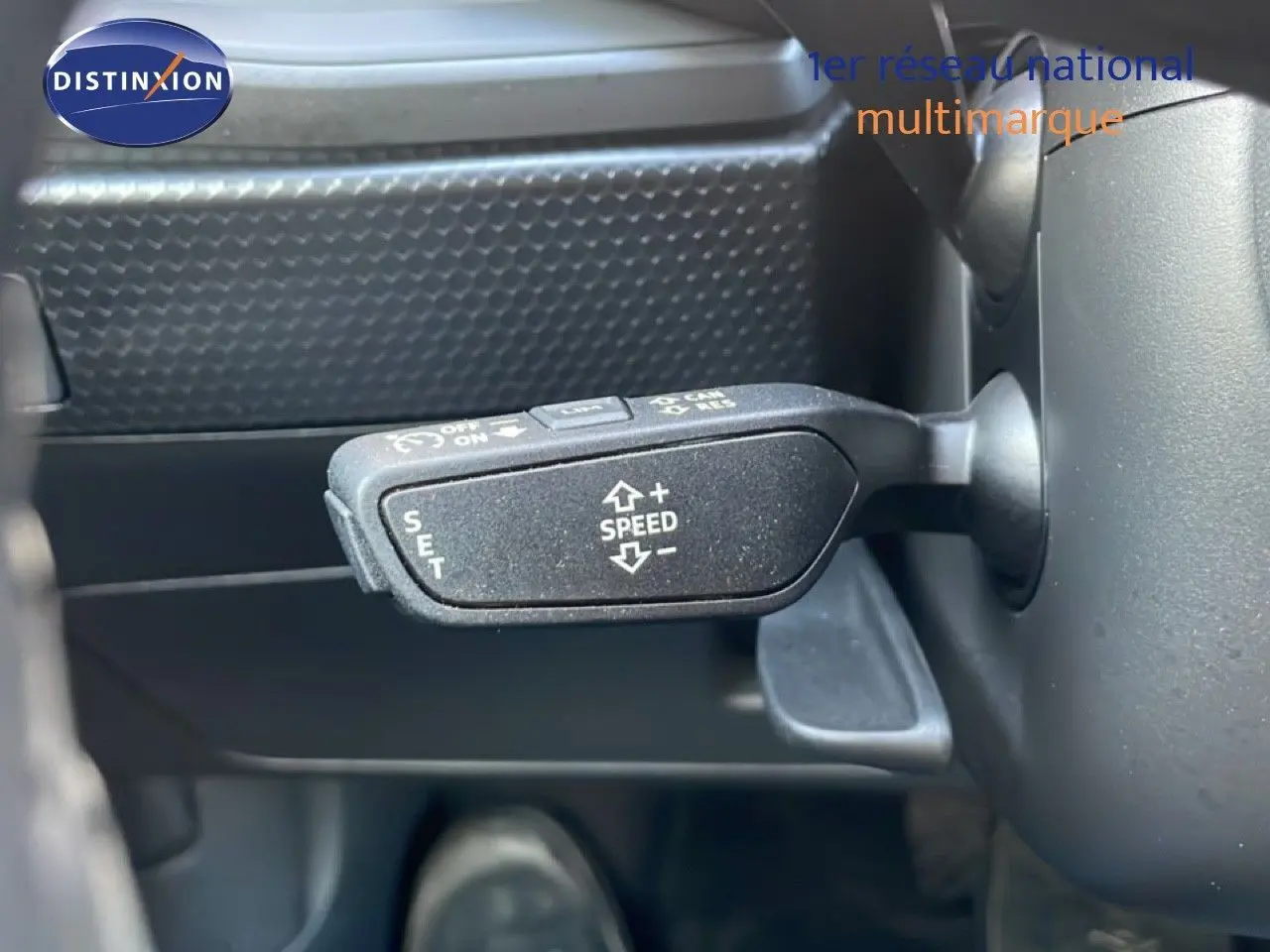 Gros plan sur la commande de régulateur de vitesse à gauche du volant dans l'Audi A1 Sportback blanc glacier 2023.