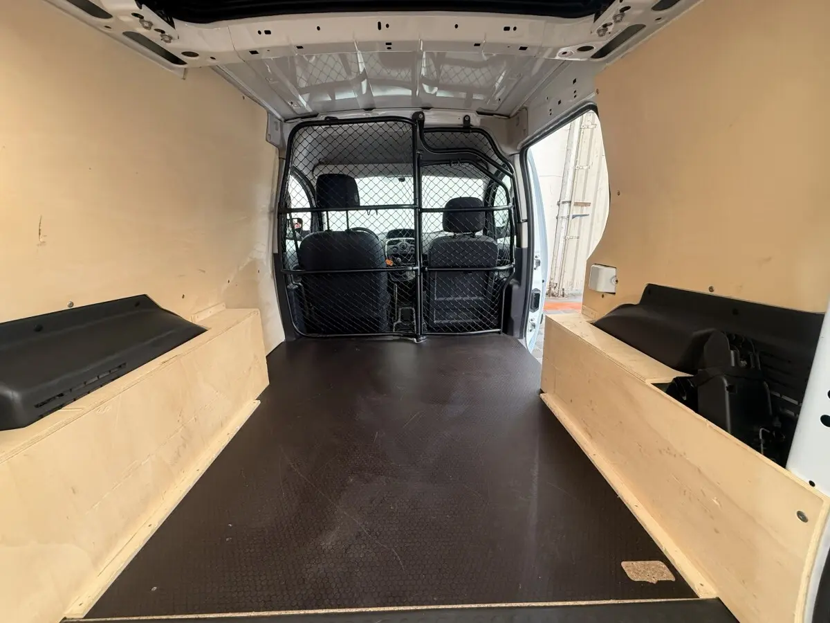 Vue intérieure arrière du Renault Kangoo blanc 2016, montrant l'espace de chargement avec cloison tubulaire noire.
