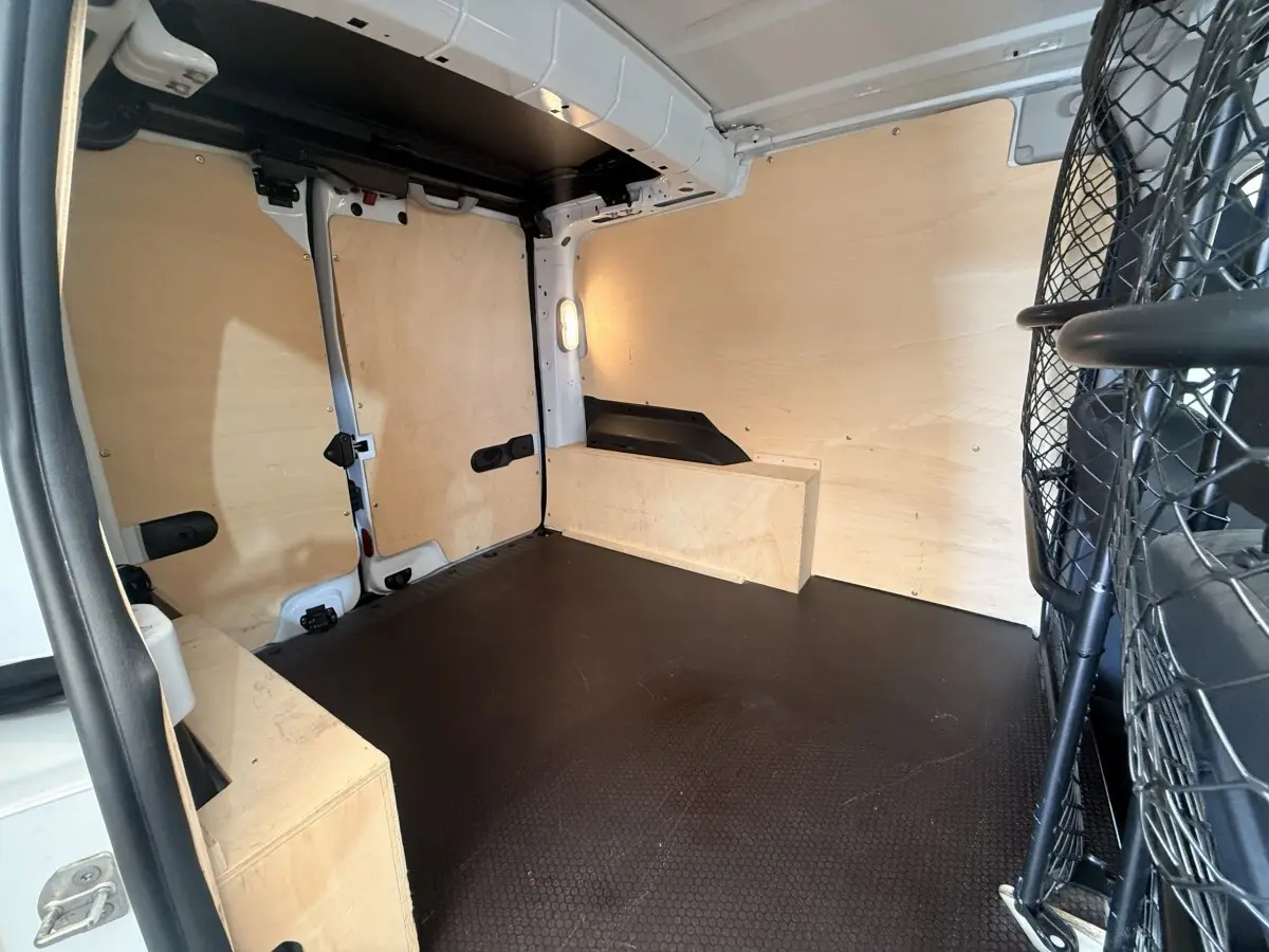 Intérieur du coffre du Renault Kangoo blanc vu de l'arrière, avec cloison tubulaire et revêtement bois clair.