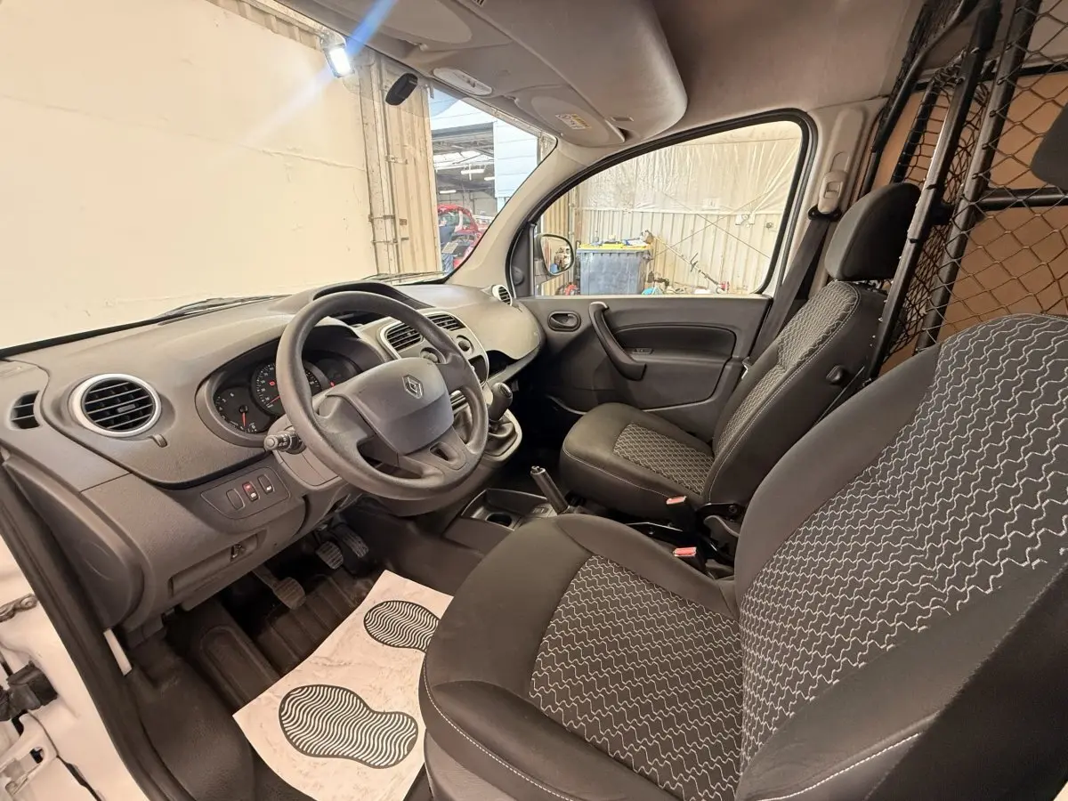 Vue intérieure côté conducteur du Renault Kangoo blanc 2016, montrant les sièges, volant et cloison tubulaire.