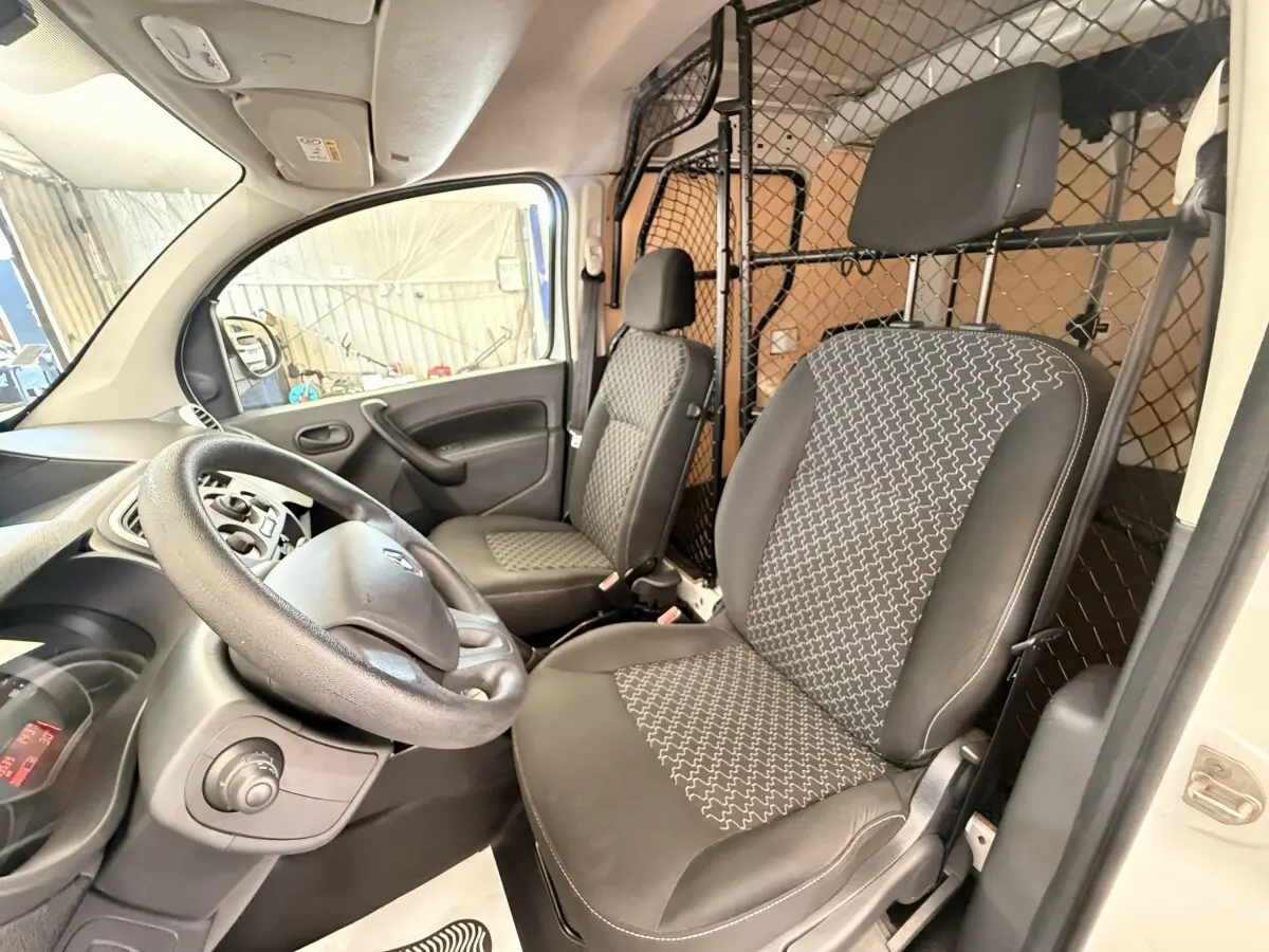 Vue intérieure côté conducteur du Renault Kangoo blanc 2016 avec cloison tubulaire pleine et sièges tissu noir à motifs.