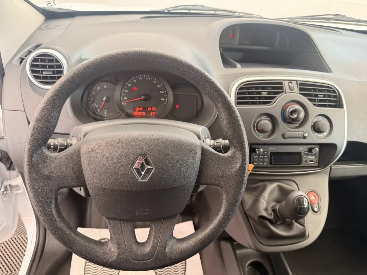 Vue intérieure centrée sur le volant et tableau de bord du Renault Kangoo blanc avec levier de vitesse manuel.