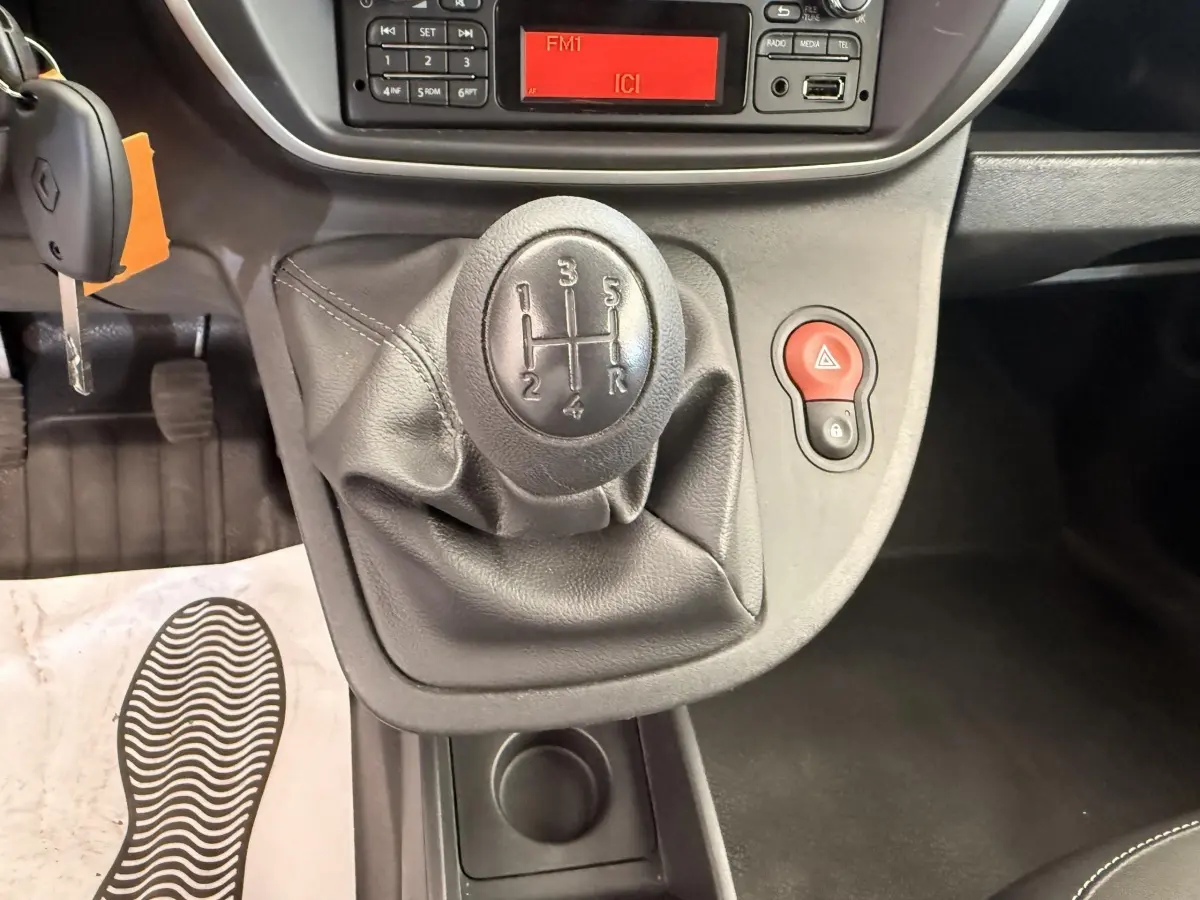 Gros plan sur le levier de vitesses manuel noir du Renault Kangoo Confort Energy dCi 75, avec tableau de bord et bouton de warning rouge visible.