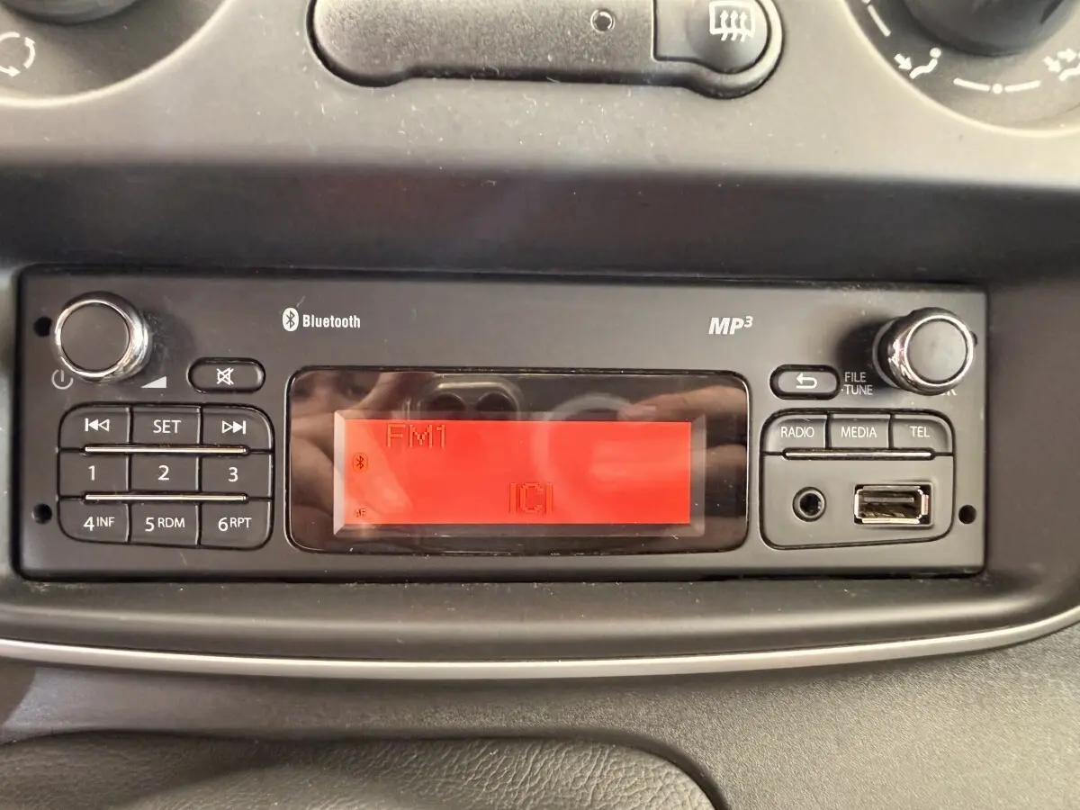 Gros plan sur la radio MP3 avec écran rouge et commandes Bluetooth du tableau de bord du Renault Kangoo blanc.