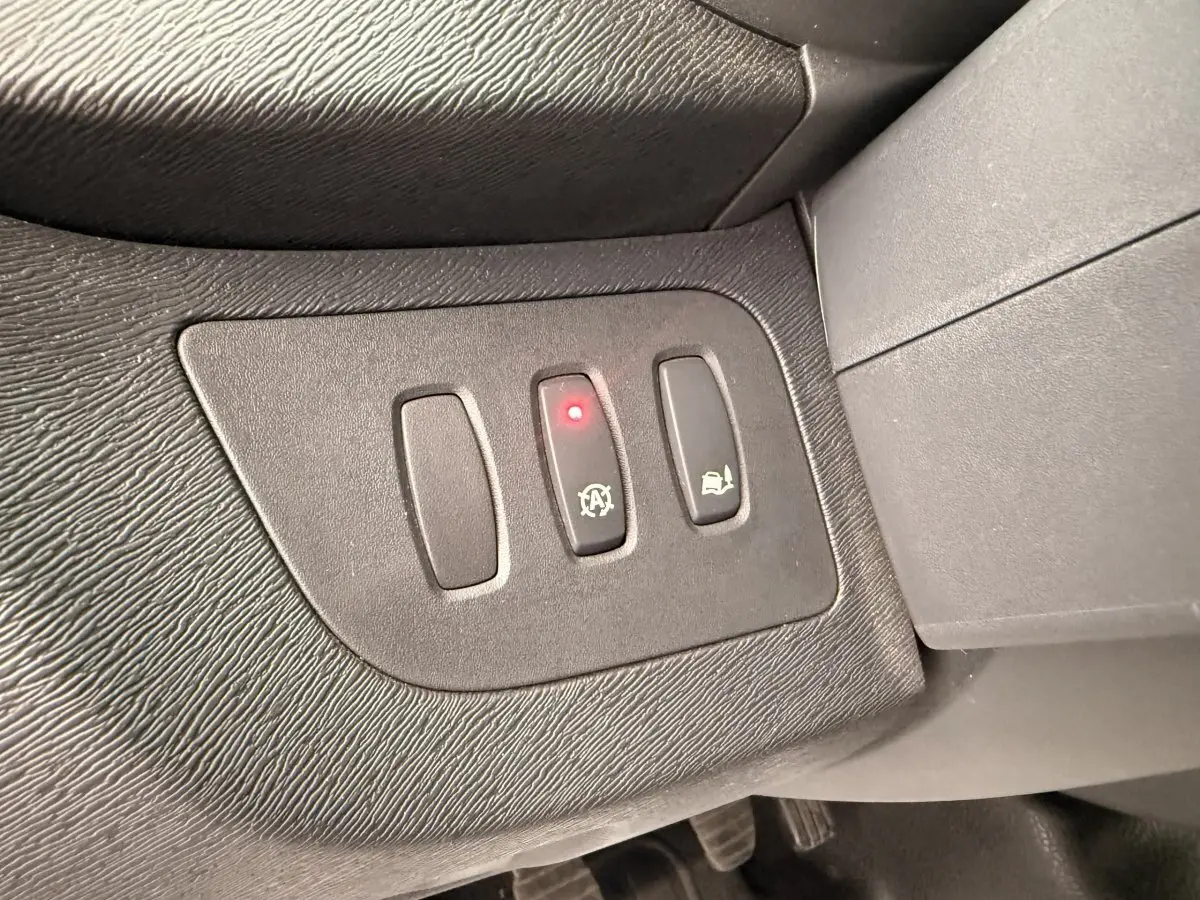 Gros plan sur les boutons de commande noirs du tableau de bord du Renault Kangoo blanc, avec témoin lumineux rouge allumé.