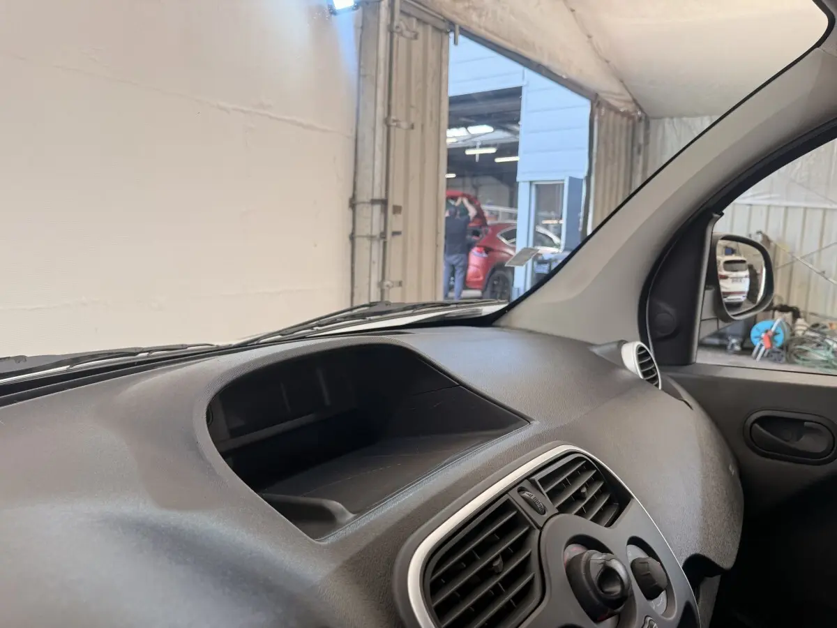 Vue intérieure côté passager du tableau de bord noir du Renault Kangoo blanc, avec prise d'air et porte.