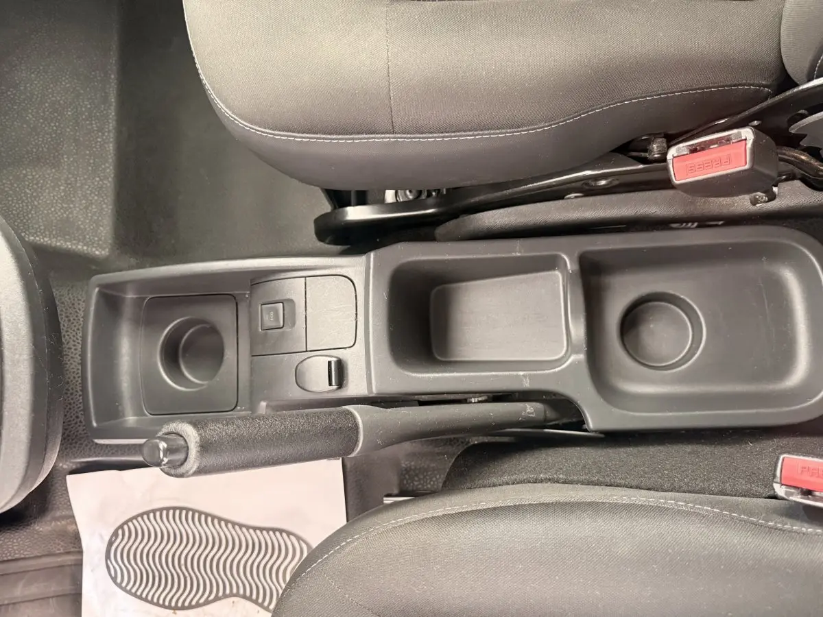 Vue plongeante sur la console centrale noire entre les sièges avant du Renault Kangoo blanc, frein à main et rangements visibles.
