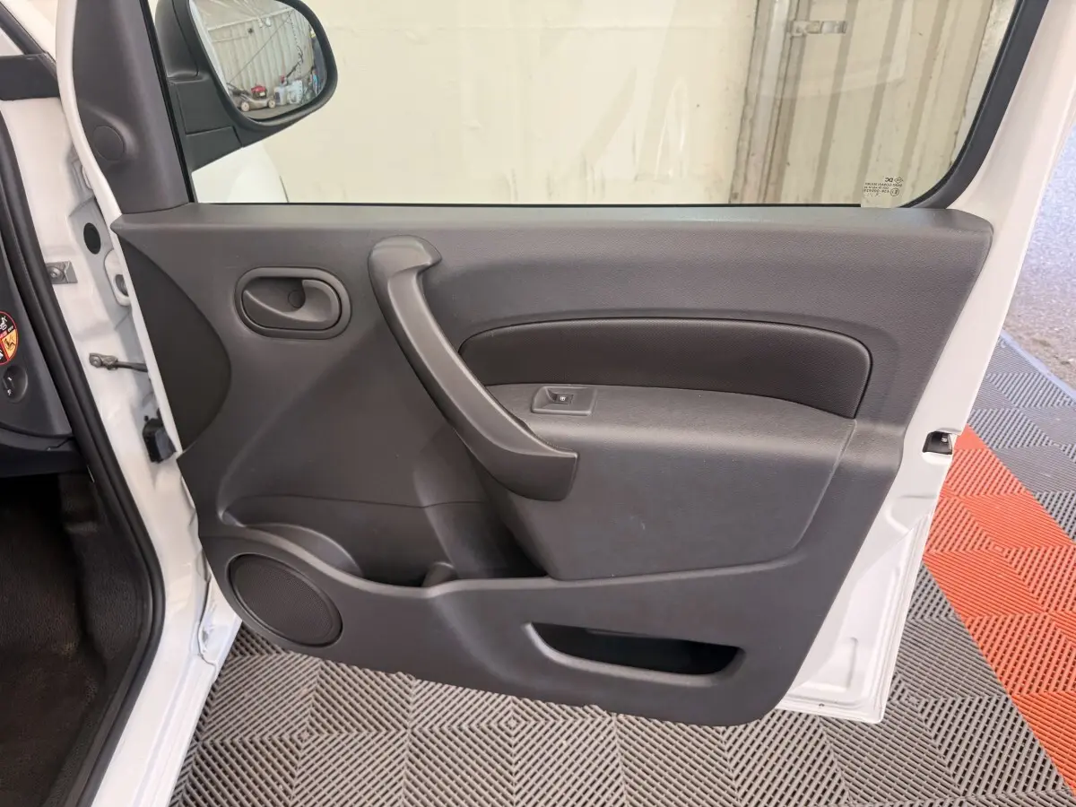 Vue intérieure de la porte avant gauche du Renault Kangoo blanc, avec poignée et commande de vitre électrique.