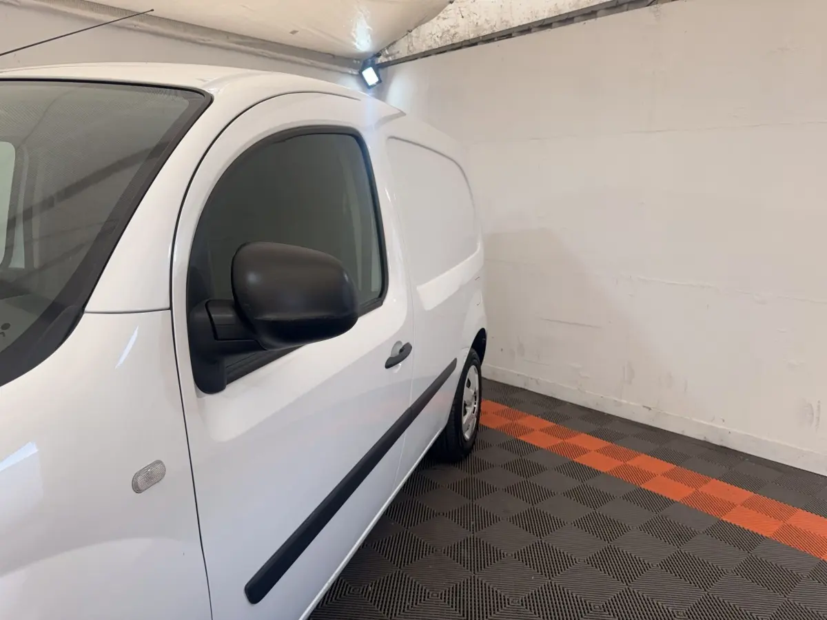 Vue de profil côté gauche d’un Renault Kangoo blanc 2016 en intérieur avec rétroviseurs noirs et bande latérale noire.