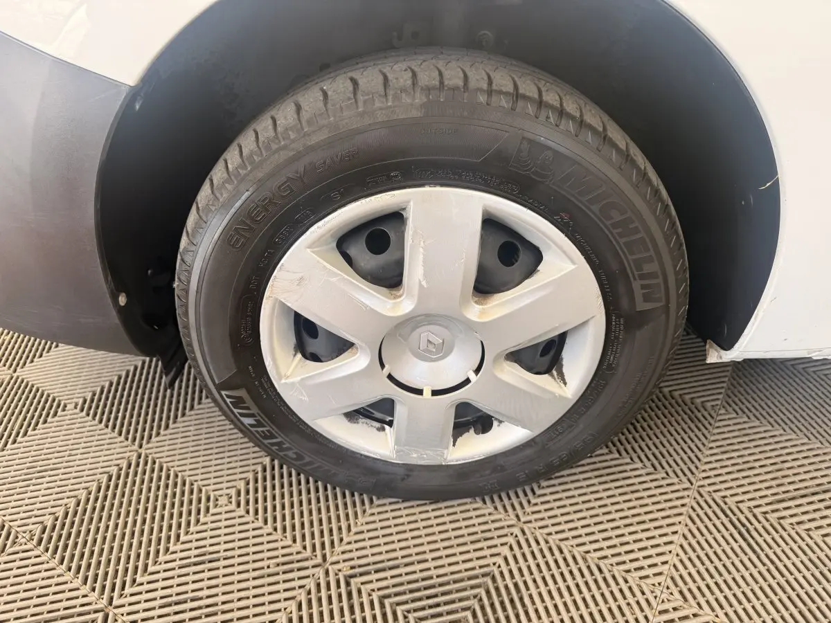 Gros plan sur la roue avant gauche d’un Renault Kangoo blanc avec jante acier et enjoliveur abîmé.