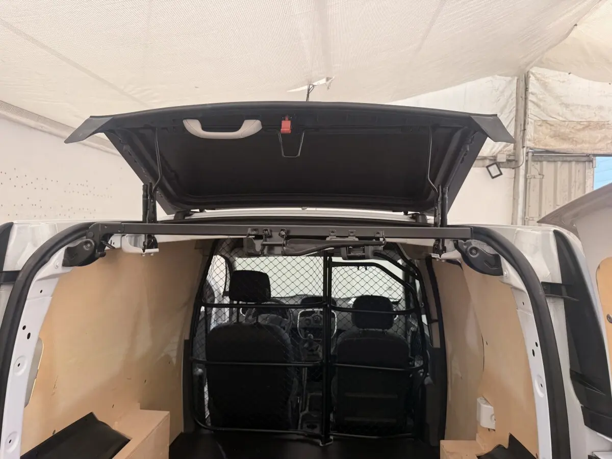 Vue arrière du Renault Kangoo blanc 2016 avec porte ouverte et cloison tubulaire pleine visible à l'intérieur.