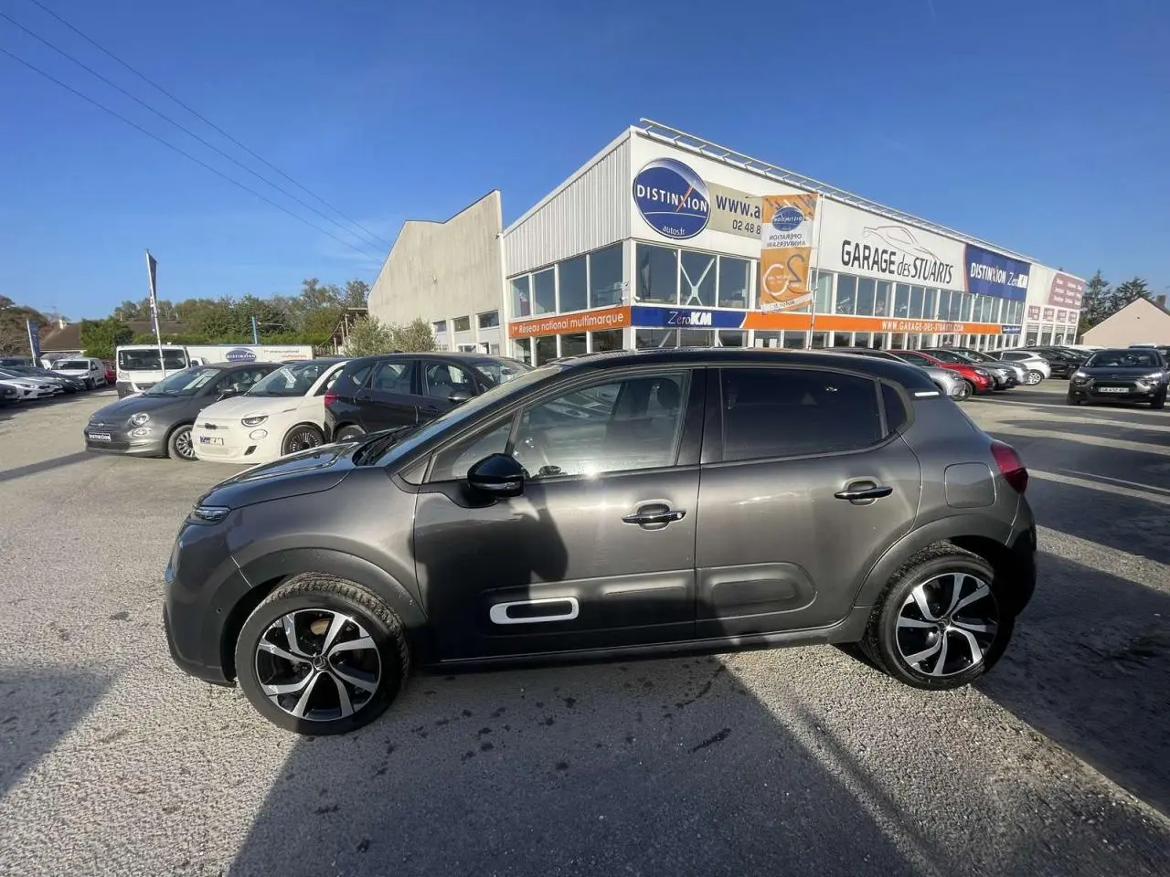Profil droit d'une Citroën C3 2021 gris foncé avec toit noir et jantes alliage diamantées sur parking extérieur.