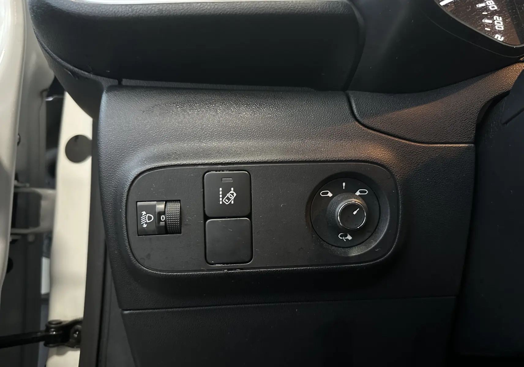 Vue intérieure côté gauche du tableau de bord d'une Citroën C3 blanche, avec commandes de réglage des phares et des rétroviseurs.