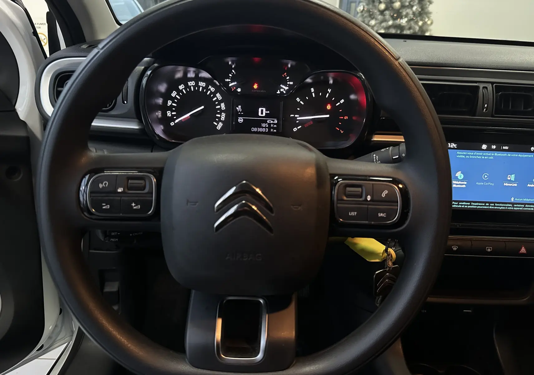 Vue intérieure centrée sur le volant noir de la Citroën C3 blanche, avec tableau de bord et écran tactile visibles.