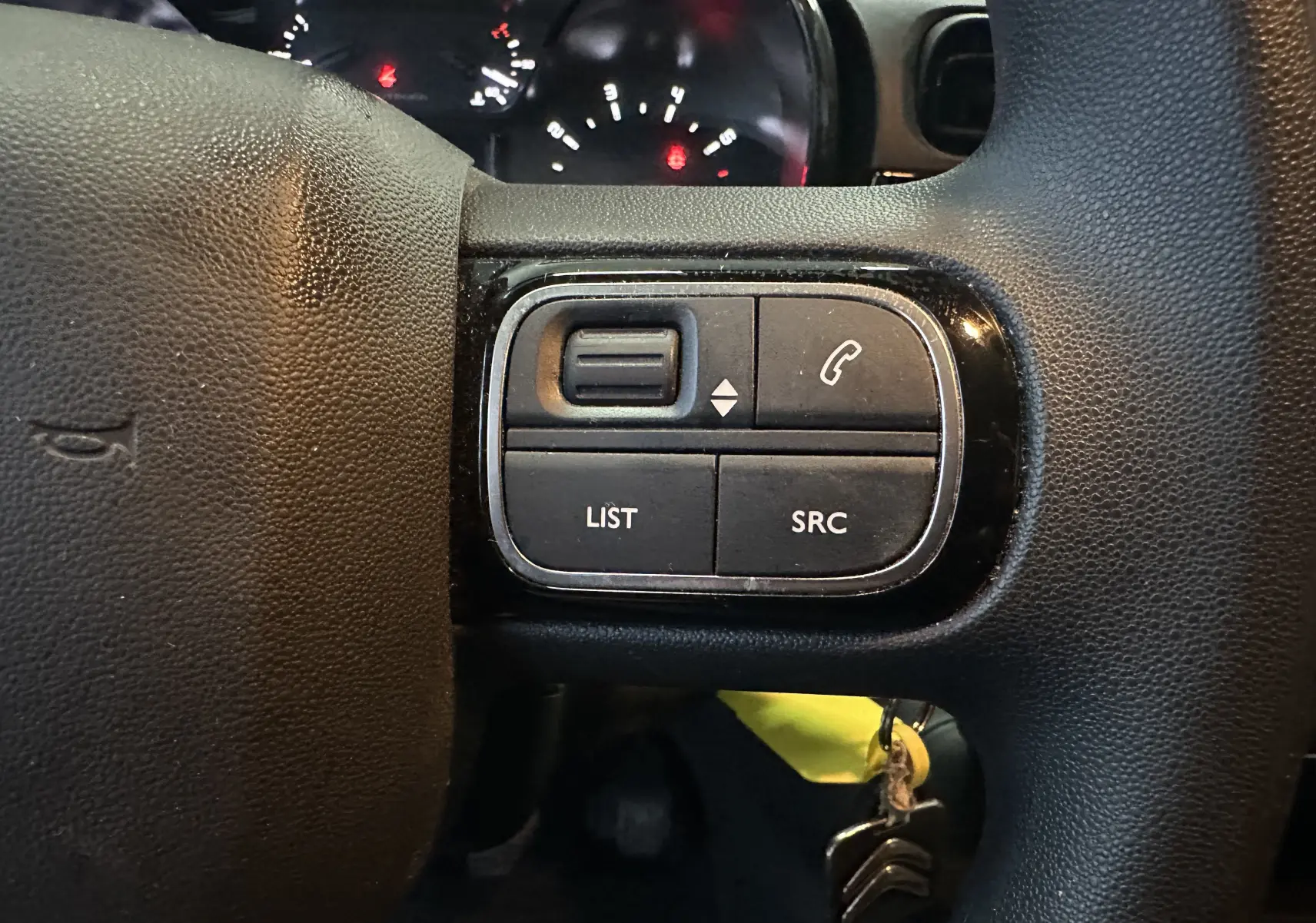 Gros plan sur les commandes multifonctions à gauche du volant noir d’une Citroën C3 blanche de 2018.