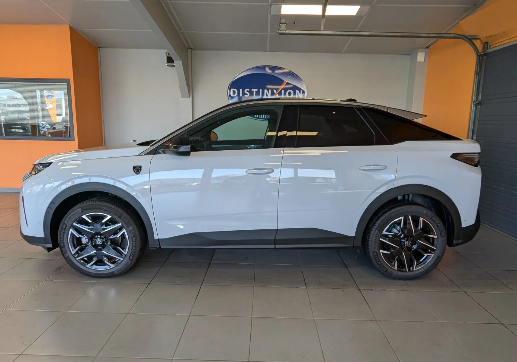 Vue latérale gauche d’un Peugeot 3008 blanc Okenite avec toit noir et jantes alliage bicolores en intérieur showroom.