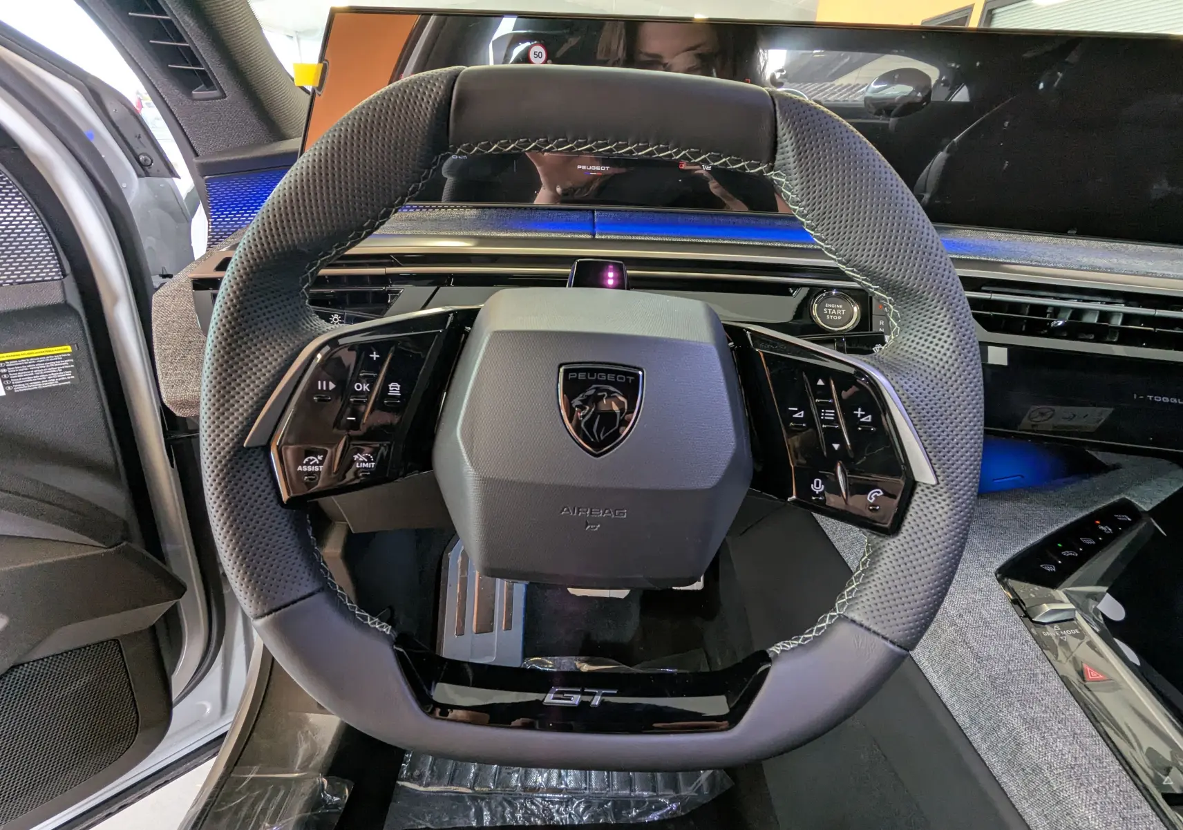 Vue rapprochée du volant GT du Peugeot 3008 blanc Okenite, avec tableau de bord numérique et commandes intégrées.