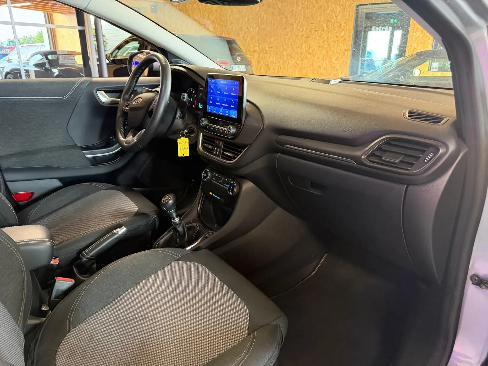 Vue intérieure côté conducteur du Ford Puma gris 2021, avec tableau de bord noir et écran tactile central allumé.