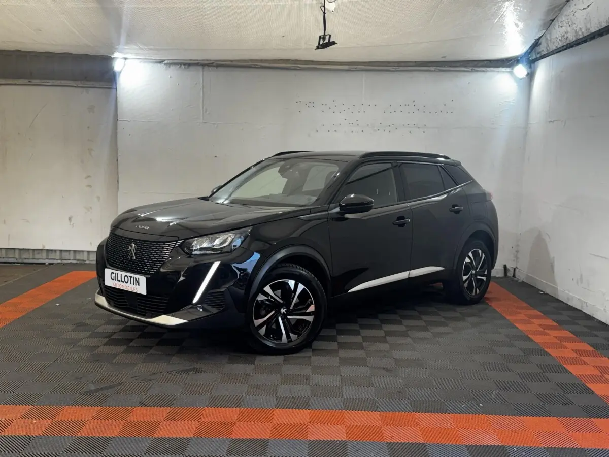 Peugeot 2008 noir en 3/4 avant droit, avec jantes alliage bicolores et feux LED distinctifs, stationné en intérieur.