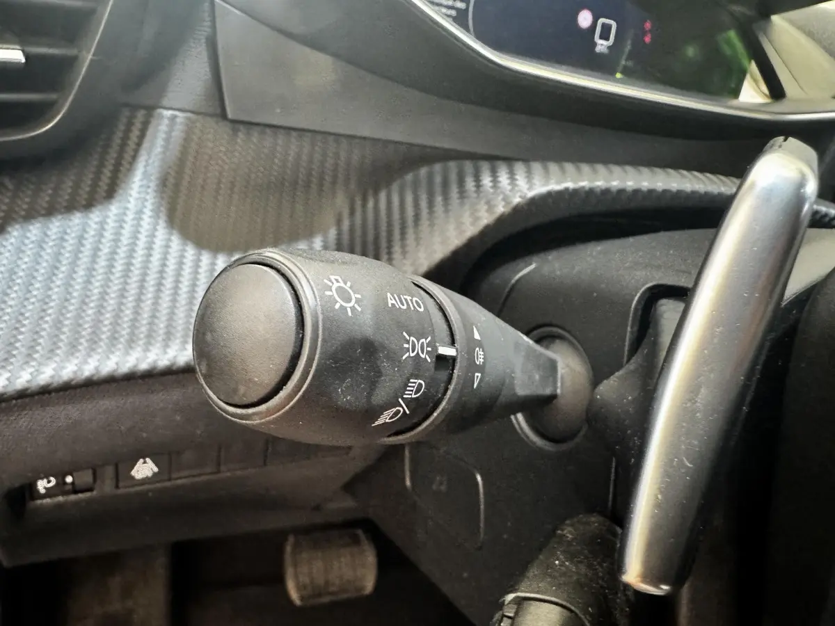 Gros plan sur la commande des phares à gauche du volant dans l’habitacle noir du Peugeot 2008 2022.