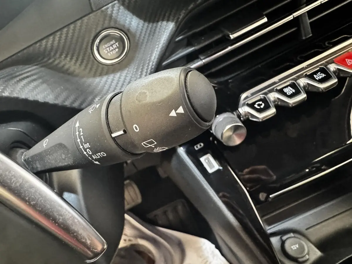 Gros plan sur la commande d’essuie-glace et le bouton démarrage d’un Peugeot 2008 noir, intérieur moderne avec finition carbone.