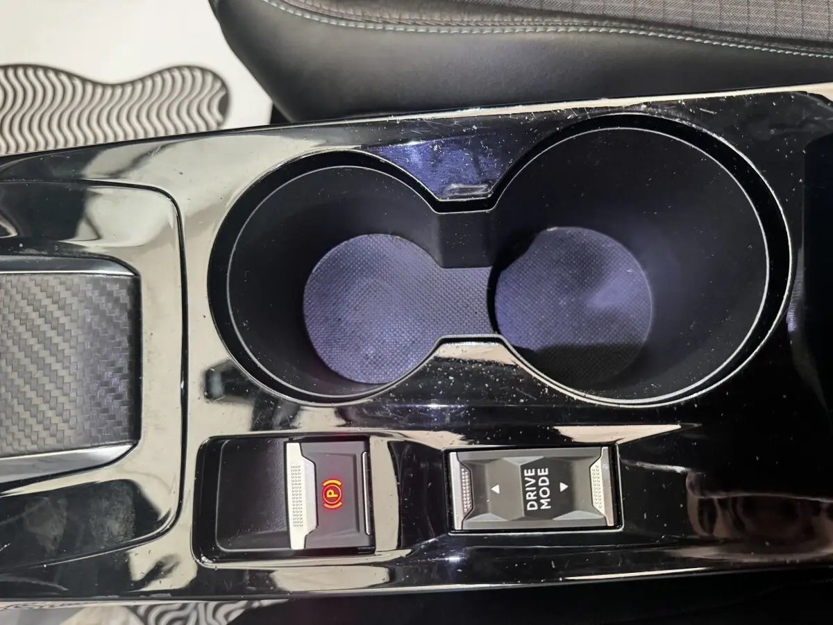 Gros plan sur la console centrale noire du Peugeot 2008, avec porte-gobelets et boutons frein électrique et mode de conduite.