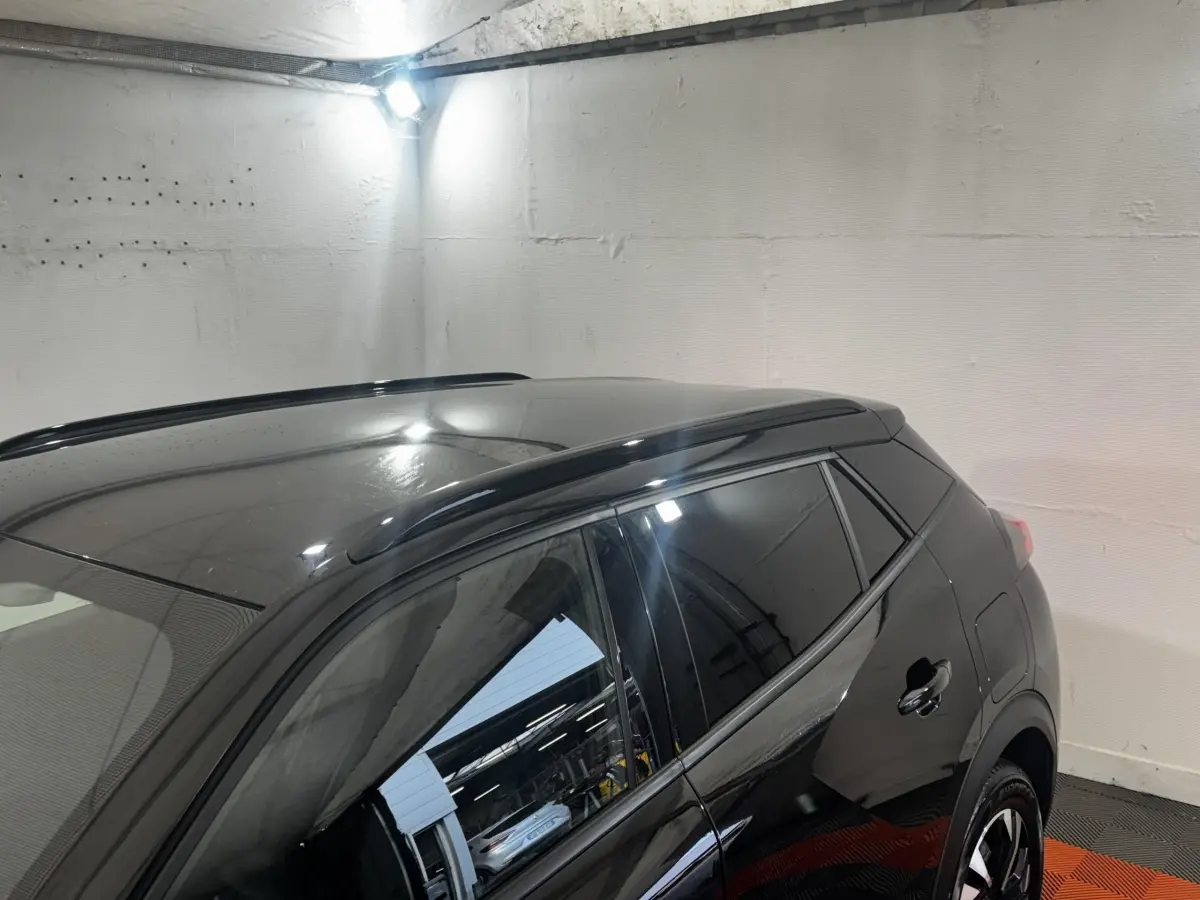 Vue latérale droite d’un Peugeot 2008 noir brillant avec vitres teintées et barres de toit dans un garage.