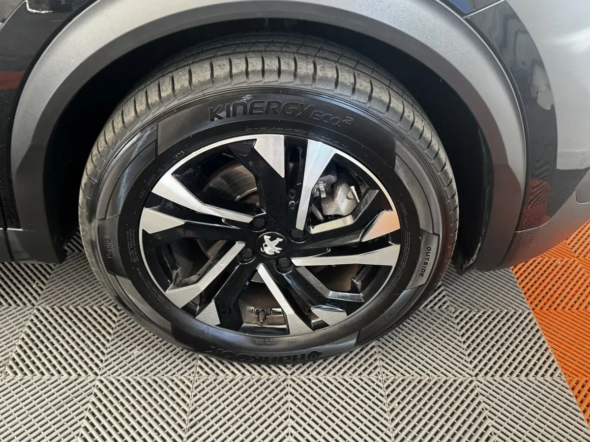 Gros plan sur la roue avant droite noire du Peugeot 2008 2022 avec jante alliage bicolore et logo lion central.