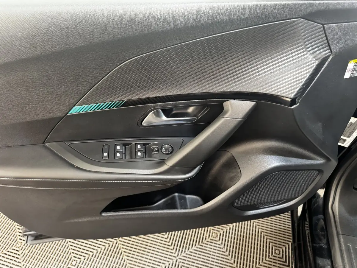 Vue rapprochée de la porte avant gauche noire du Peugeot 2008 2022 avec insert décoratif carbone et commandes électriques.
